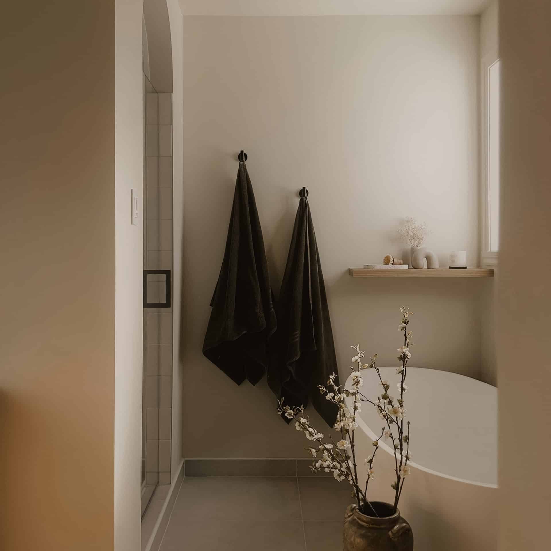 Jolie salle de bain minimaliste avec un vase de fleurs et des serviettes noires.