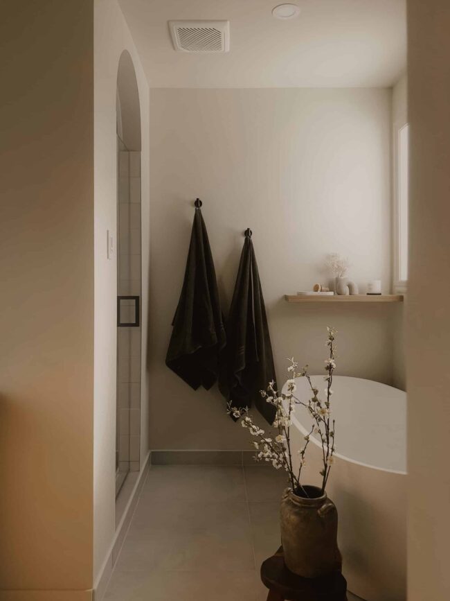 Jolie salle de bain minimaliste avec un vase de fleurs et des serviettes noires.
